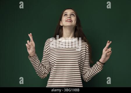 Una donna è in piedi di fronte a un muro verde vibrante. Lei appare contemplativa mentre guarda in lontananza. Il contrasto tra la sua figura e la Foto Stock