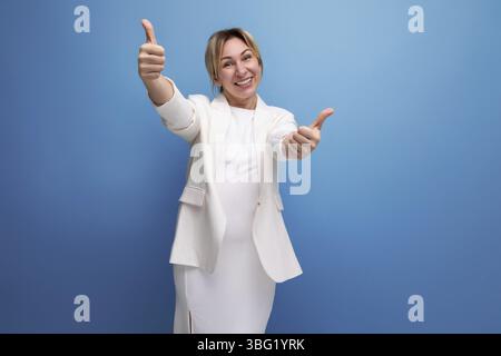Elegante giovane donna europea bionda vestita con una giacca bianca e vestito su uno sfondo isolato Foto Stock