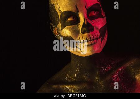 Isolata sul nero, foto ravvicinata, tonificata di rosso e giallo, bella giovane donna bionda caucasica con arte del corpo scull, occhi grigi Foto Stock