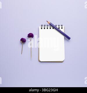 Taccuino vuoto, matita colorata, fiori secchi su sfondo viola. Vista dall'alto, spazio per la copia Foto Stock