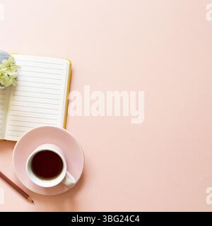 Taccuino aperto, tazza di tè, fiori secchi su sfondo rosa. Vita quotidiana, spazio di lavoro, concetto di studio Foto Stock
