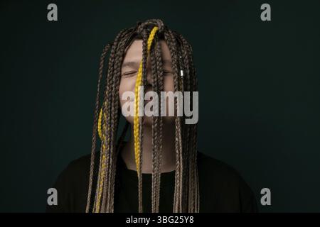 Una donna con lunghi dreadlock si trova di fronte a uno sfondo verde vivace. I suoi capelli cadono sulla schiena mentre posa con sicurezza per il venuto Foto Stock
