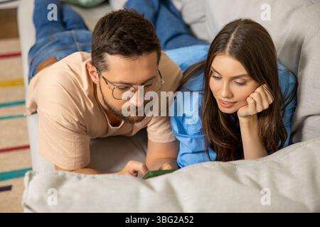 Giovane donna felice e uomo che usano lo smartphone insieme sdraiati sul divano Foto Stock