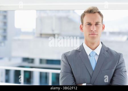 Uomo grigio in piedi accanto alla ringhiera del balcone che guarda fiducioso con cravatta azzurra e spazio fotocopie Foto Stock