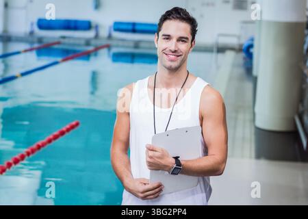 Pullman da nuoto maschile in piedi a bordo piscina con appunti che indossa fischio vicino ai divisori di corsia Foto Stock
