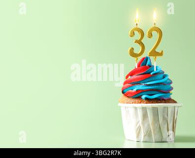 Delizioso cupcake con candele a forma di numeri accesi su sfondo turchese chiaro, spazio per il testo. 32° compleanno o altra occasione speciale Foto Stock