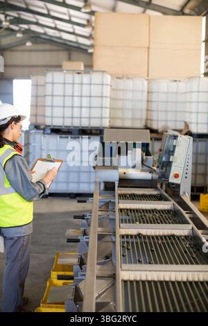 Nastro trasportatore per il trasporto di oggetti scuri sotto luci ad alloggiamento alto in fabbrica, con contenitori IBC Foto Stock