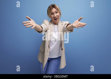 La bionda sorridente, giovane adulto in giacca, si abbraccia sullo sfondo dello studio Foto Stock