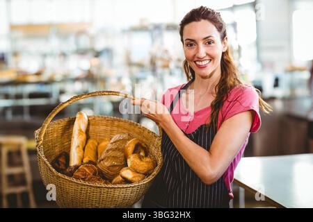 Lavoratrice di panificio che tiene in mano un cesto di tessuti riempito con pane assortito all'interno del negozio di panetteria Foto Stock
