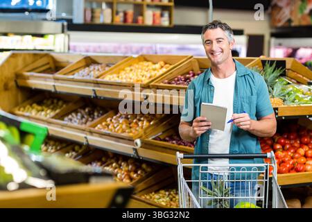 Uomo maturo che scrive con una penna sul blocco note accanto al carrello nella sezione prodotti, spazio copia Foto Stock