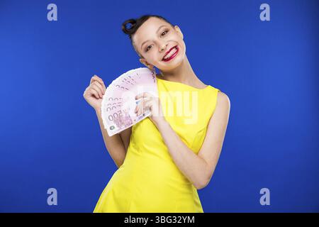 Ragazza con un sacco di soldi in un vestito giallo in stile retrò Foto Stock