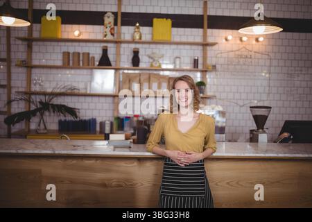 Barista donna che indossa una camicetta e un grembiule che aziona la macchina per caffè espresso e il terminale POS al bar Foto Stock