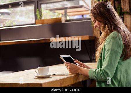 Tablet che mostra i contenuti e si appoggia sul bancone di legno accanto allo smartphone e alla tazza di caffè in caffetteria Foto Stock
