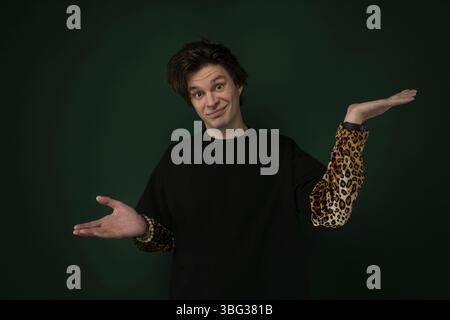 Un uomo che indossa una camicia nera sta in piedi con le mani estese verso l'esterno di fronte a lui. Sembra che stia tenendo qualcosa o stia cercando di trasmettere un messaggio Foto Stock
