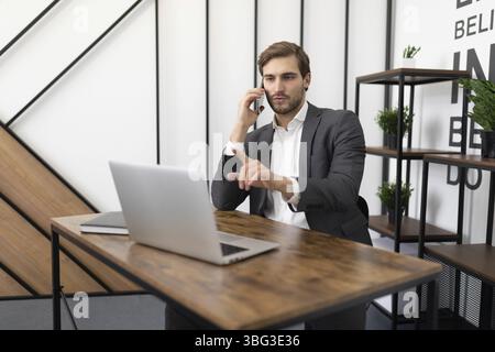 Un avvocato impegnato che parla al telefono in ufficio con un cliente e guarda un portatile Foto Stock