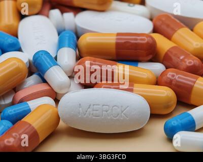 Pillola bianca con impronta MERCK posta su un mucchio di compresse e capsule colorate in una vista farmaceutica. Foto Stock