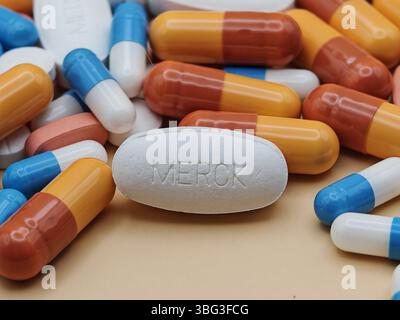 Pillola bianca con impronta MERCK posta su un mucchio di compresse e capsule colorate in una vista farmaceutica. Foto Stock