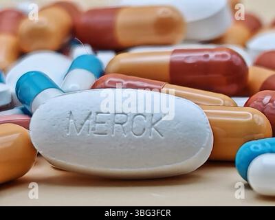 Pillola bianca con impronta MERCK posta su un mucchio di compresse e capsule colorate in una vista farmaceutica. Foto Stock