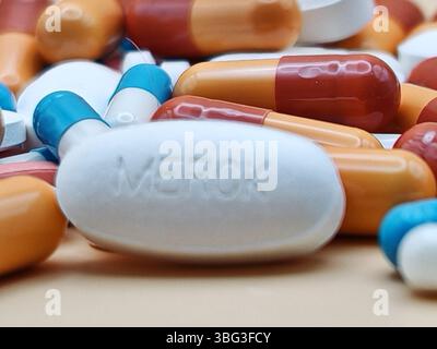 Pillola bianca con impronta MERCK posta su un mucchio di compresse e capsule colorate in una vista farmaceutica. Foto Stock