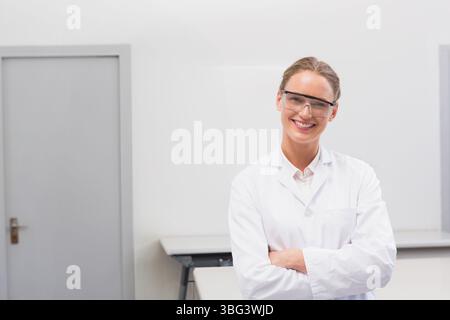 Scienziata che sorride mentre si trova in un laboratorio pulito, indossa un camice da laboratorio e occhiali di sicurezza Foto Stock