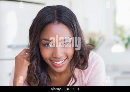 Donna afroamericana che si appoggia in avanti toccando il viso sorridente alla macchina fotografica in cucina con i fiori Foto Stock