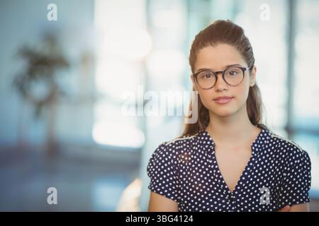 Donna che indossa occhiali da vista e camicetta a pois in piedi nello spazio di coworking con piante in vaso Foto Stock