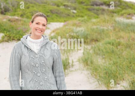 Donna anziana che indossa un cappotto grigio in maglia a cavo, un maglione in maglia in piedi sul percorso delle dune, copia spazio Foto Stock