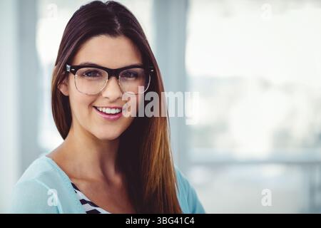Donna con lunghi capelli marroni che indossa occhiali da vista con bordo nero sorridente e che guarda la fotocamera in ufficio Foto Stock