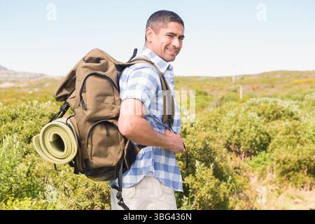 Uomo adulto maturo in piedi nella macchia mediterranea con zaino con olive e tappetino per dormire, spazio per copiare Foto Stock