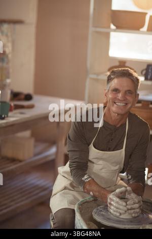 vasaio maschio senior che forma l'argilla su ruota in ceramica in officina con utensili in argilla sul banco di lavoro Foto Stock