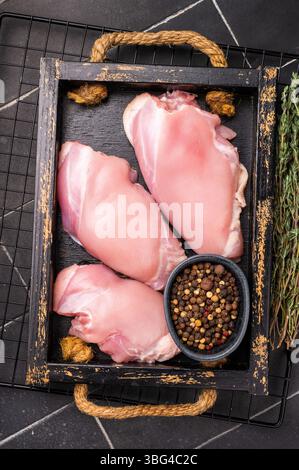 Filetti di cosce di pollo crude in un vassoio di legno fondo nero. vista dall'alto. Foto Stock