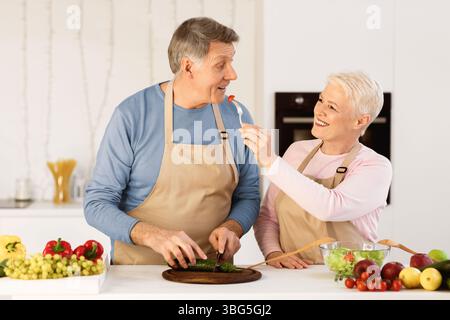 Sposi invecchiati cucinare degustazione cibo che si nutrire a vicenda in cucina Foto Stock