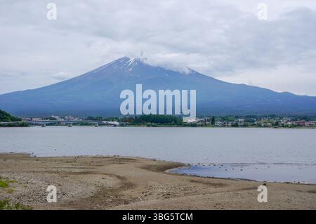 Una vista maestosa del Monte Fuji, parzialmente avvolta da nuvole, sorge sopra le calme acque del Lago Kawaguchiko. Il tranquillo paesaggio offre un ambiente tranquillo Foto Stock