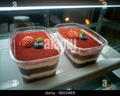Goditi queste deliziose tazze da dessert in velluto rosso ricoperte di panna, ricoperte di fragole e mirtilli, perfette per qualsiasi occasione dolce. Foto Stock