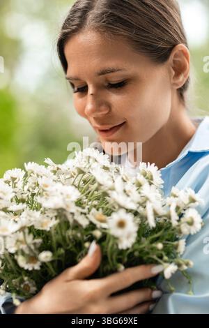 Flowers Woman Daisies: Una ragazza sorridente tiene le margherite in un ambiente all'aperto illuminato dal giorno, apprezzandone la bellezza. Foto Stock