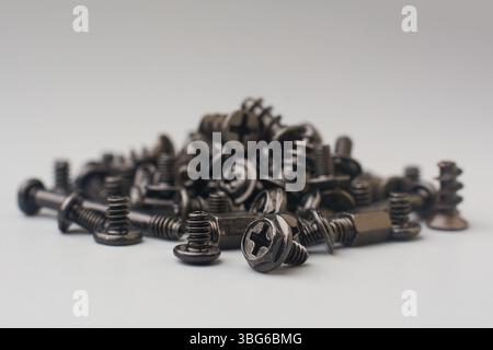 pila di viti di colore scuro sparse su una superficie di sfondo grigia, dispositivi di fissaggio per computer con testa piatta e a croce phillips Foto Stock