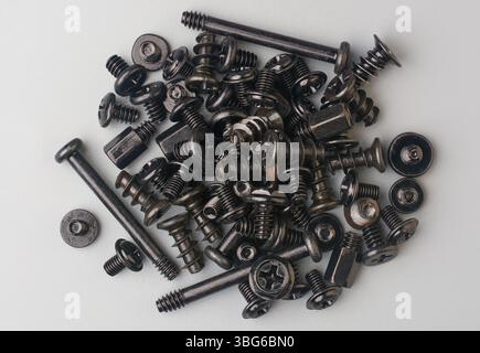 pila di viti di colore scuro sparse su una superficie di sfondo grigia, dispositivi di fissaggio per computer con testa piatta e a croce phillips Foto Stock