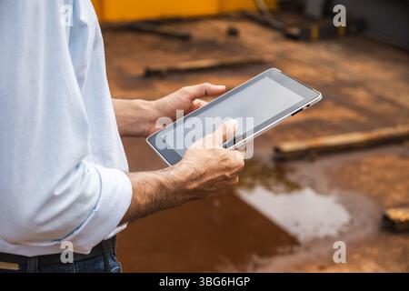 Primo piano ingegnere edile lavoratore maschio che tiene a mano un tablet computer che lavora in cantiere per la tecnologia di ispezione di progetti di indagine Foto Stock