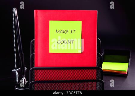 FAI IN MODO CHE CONTINO le parole scritte su un adesivo verde su un libro aziendale rosso su sfondo nero. Foto Stock