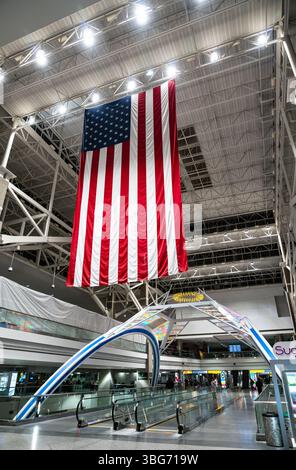 Denver, Colorado - 23 maggio 2025: L'enorme bandiera americana è appesa sopra un arco colorato e il passaggio pedonale all'interno dell'aeroporto internazionale di Denver, mentre i viaggiatori attraversano il terminal notturno illuminato. Foto Stock