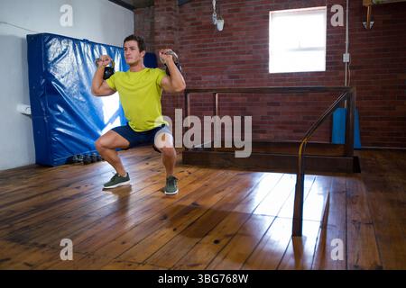 Uomo che esegue squat ponderati tenendo i manubri all'interno della palestra con telaio riformatore Pilates, spazio fotocopie Foto Stock