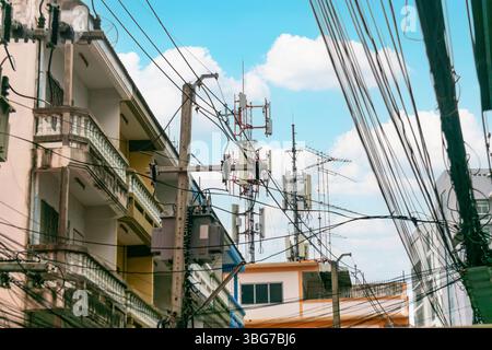 Una vibrante scena urbana caratterizzata da torri di comunicazione tra edifici e linee elettriche, che mostrano l'intersezione tra tecnologia e vita cittadina sotto una b Foto Stock