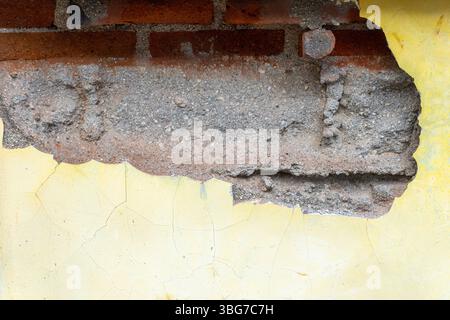 Muro con un foro e una vernice gialla e bianca. Il muro è fatto di mattoni Foto Stock