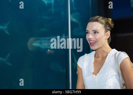 Donna adulta in piedi davanti alla vasca dell'acquario con borsa a spalla, osservando le silhouette dei pesci, copiando lo spazio Foto Stock