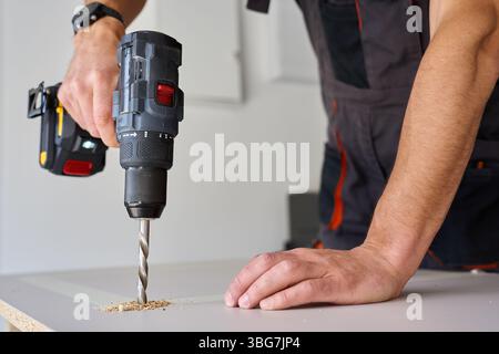 Mani maschili per la foratura di pannelli in legno con trapano elettrico. Processo di falegnameria che lavora in officina a casa, praticare fori nel truciolato Foto Stock