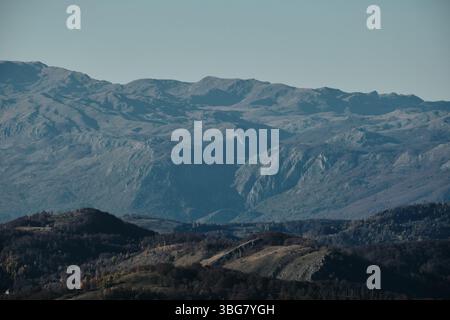 Spettacolare vista dei monti Komovi in Montenegro durante l'autunno, con ripide creste rocciose e pendii erbosi illuminati dal sole sotto un cielo azzurro. Foto Stock