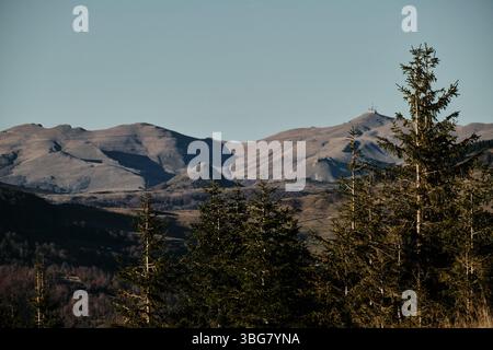 Un panoramico paesaggio autunnale sulle montagne Komovi del Montenegro, caratterizzato da strati di colline boscose e lontane vette rocciose sotto un cielo azzurro Foto Stock