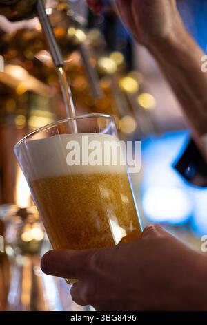 Il barista versa birra alla spina fresca nel bicchiere dal rubinetto al bar con illuminazione soffusa Foto Stock