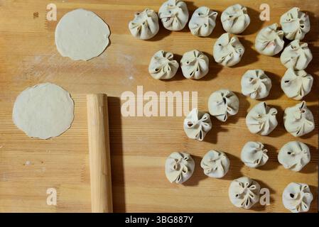 Gnocchi di buuz mongoli appena fatti disposti su un asse di legno accanto a un mattarello e cerchi di impasto, pronti per la cottura Foto Stock
