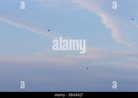 Tre mongolfiere in un vasto cielo blu con morbide nuvole, che creano un'atmosfera serena e tranquilla. Foto Stock